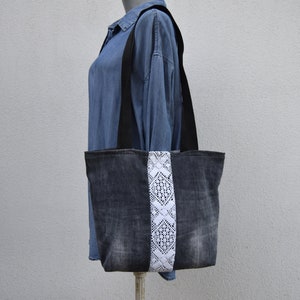 May include: A black denim tote bag with a white lace trim. The bag has black straps and is made of recycled denim.