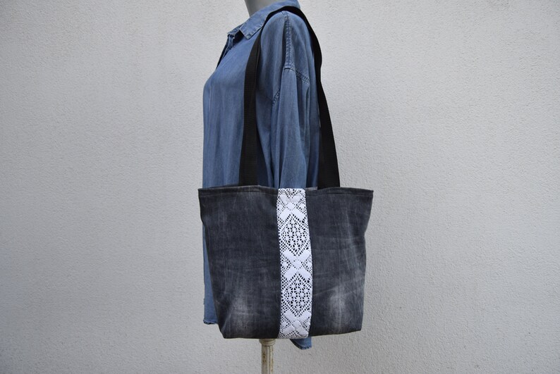 May include: A black denim tote bag with a white lace trim. The bag has black straps and is made of recycled denim.