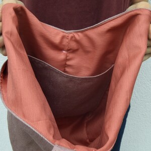 May include: A large, brown tote bag with a coral-colored lining. The bag has a single pocket on the inside.
