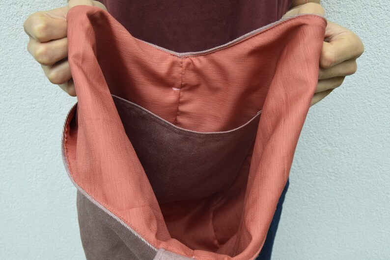 May include: A large, brown tote bag with a coral-colored lining. The bag has a single pocket on the inside.