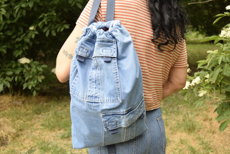 May include: A blue denim drawstring backpack with multiple pockets and a blue strap.