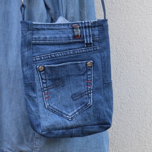 Puede incluir: Bolso cruzado de mezclilla azul con un bolsillo y detalles de costura rojos. El bolso est&aacute; hecho de jeans reciclados y presenta los detalles originales del bolsillo y la trabilla. El bolso se suspende con una correa fina.