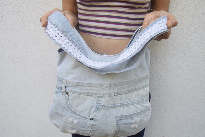 May include: A light blue denim tote bag with a white lace trim. The bag is made from recycled denim and has a spacious interior.
