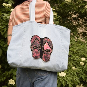 May include: A light blue denim tote bag with two pink and black flip-flop patches that say "Rio" on them.