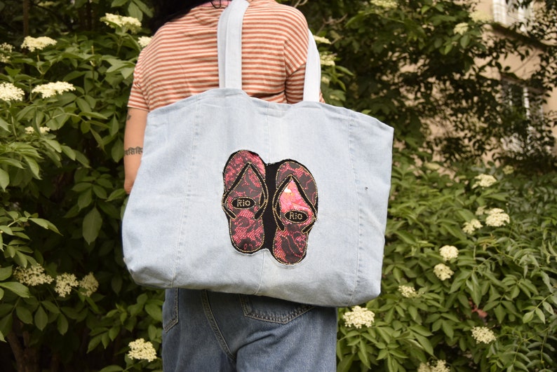 May include: A light blue denim tote bag with two pink and black flip-flop patches that say "Rio" on them.