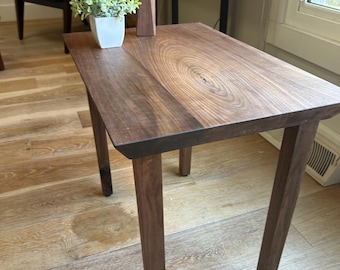 May include: A rectangular wooden side table with four legs. The tabletop features a natural wood grain pattern. A small white square pot with a green plant and a wooden candle holder are on the table.