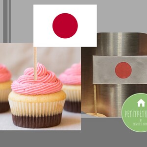 以下が含まれることがあります： ピンクと白のカップケーキが3つあり、ピンクのフロスティングがかけられています。中央のカップケーキには、日本の旗のつまようじが刺さっています。カップケーキは白い表面の上に置かれています。画像には、金属製の表面に日本の旗がアップで写っているものも含まれています。