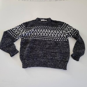 Op de afbeelding: Zwart-witte trui met geometrisch patroon en ronde hals. De trui heeft een witte band met een geometrisch patroon over de borst.
