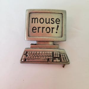 Könnte beinhalten: Eine silberfarbene Computer-förmige Anstecknadel mit der Aufschrift "mouse error!" auf dem Bildschirm. Die Anstecknadel hat unten eine Tastatur. Die Anstecknadel ist wahrscheinlich aus Metall.