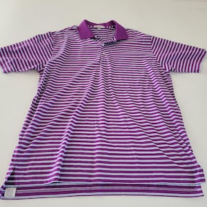 以下が含まれることがあります： 紫と白のストライプのポロシャツ。紫の襟と半袖が付いています。 シャツには3つボタンの前立てと裾に小さなタグが付いています。 シャツは軽量素材で作られています。