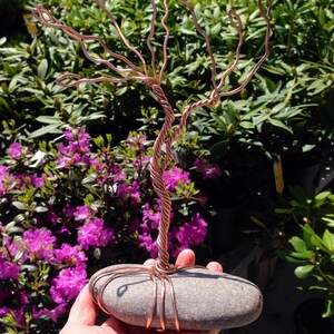 May include: A copper wire sculpture of a tree with a gray stone base. The sculpture is held in a person's hand.