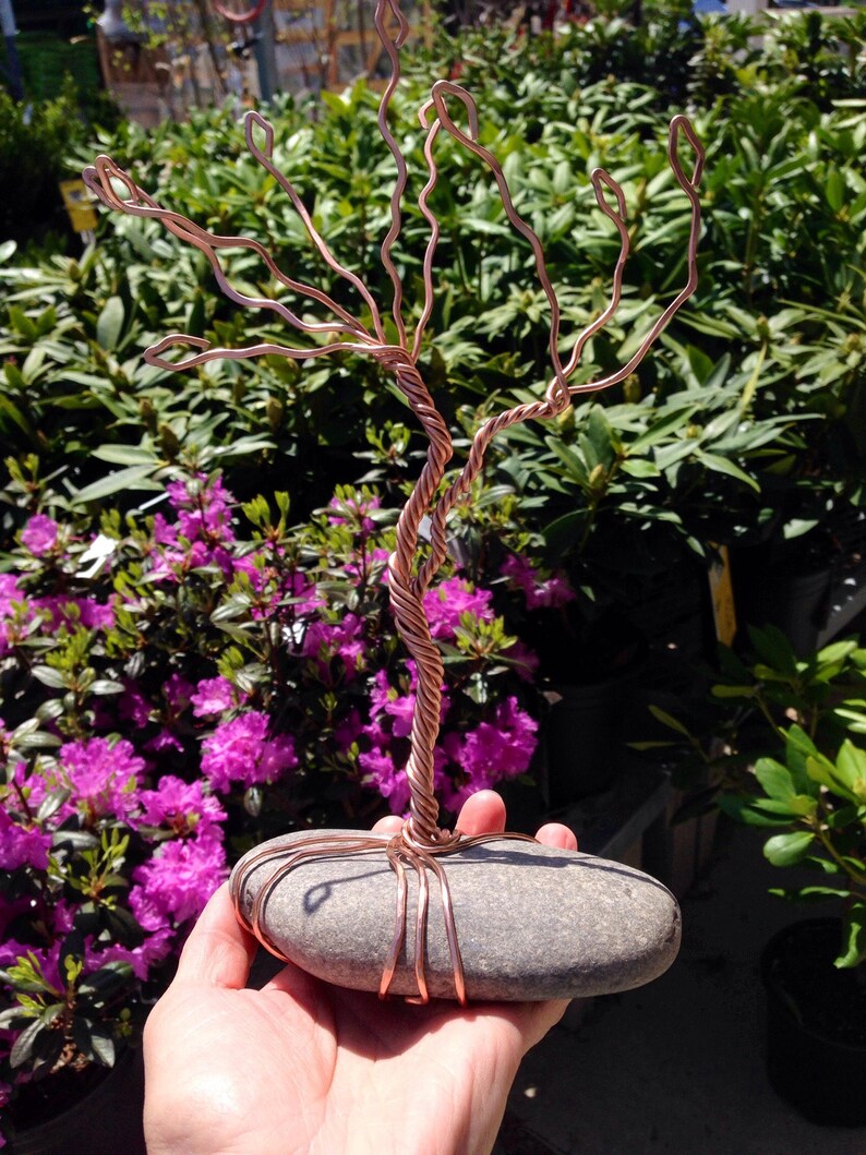 May include: A copper wire sculpture of a tree with a gray stone base. The sculpture is held in a person's hand.