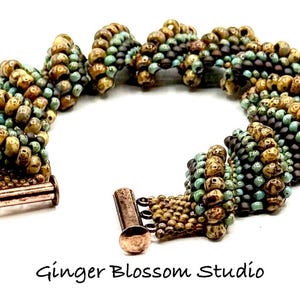 May include: A handcrafted bracelet featuring a spiral design made of small, colorful beads. The beads are in shades of gold, brown, and teal, with a copper-colored clasp. The bracelet is displayed on a white background.