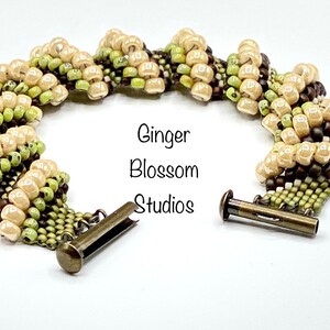 May include: A beaded bracelet with a brown, green, and cream color scheme. The bracelet has a toggle clasp.