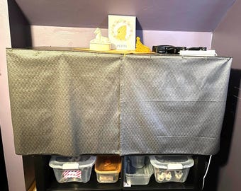 May include: A rectangular dark gray fabric cover with a repeating geometric pattern draped over a black shelving unit. The top surface holds a white figurine, a rectangular card with a yellow frog illustration and the text PERTY, and black items.