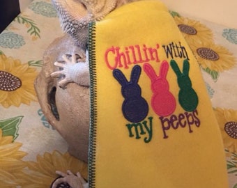 May include: A yellow blanket with the text "Chillin' With my peeps" and three bunny figures in blue, pink, and green. The blanket is draped over a bearded dragon lizard.