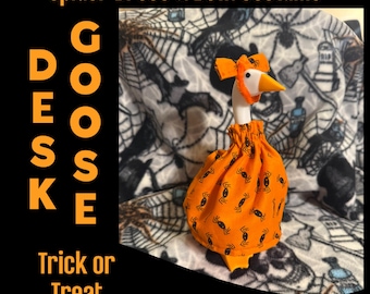 May include: A white goose figurine wearing an orange dress and matching head bow, both featuring a black spider pattern. The text on the image reads: Spider Dress & Bow/Costume, DESK GOOSE, Trick or Treat. The goose has a bright orange beak.