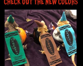 May include: Three bearded dragons wearing Crayola crayon costumes. The costumes are blue, brown, and green and have the Crayola logo and the name of the color on them. The text on the costumes reads "Draygons" and the color name.