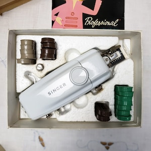 May include: A white Singer sewing machine with accessories, including bobbins and presser feet, in its original box. The box also contains a manual with the word "Professional" on it.