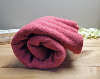 Op de afbeelding: Een opgerolde rode fleece deken. De deken is zacht en comfortabel, perfect om op de bank te knuffelen.