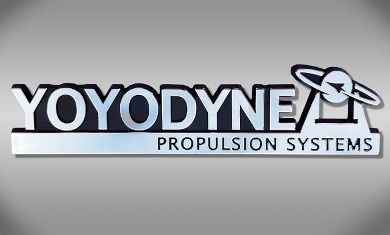 May include: A silver and black logo with the text "YOYODYNE" and "PROPULSION SYSTEMS" underneath. The logo features a stylized image of a planet with a ring around it.