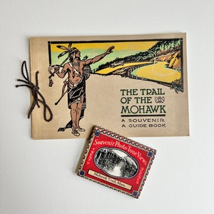 May include: A vintage guide book titled "The Trail of the Mohawk" with a drawing of a Native American man on the cover. A small red box with the text "Souvenir Photo-Tone Views" is also pictured.