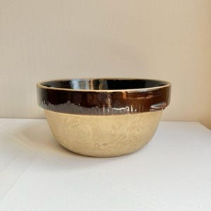 May include: A brown and beige ceramic mixing bowl with a brown rim. The bowl has a textured surface and a slightly rounded bottom.