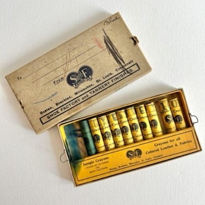 May include: A vintage box of sample crayons for colored leather and fabrics. The box is yellow with black text and a small logo. The crayons are in individual cardboard tubes with yellow and black labels. The box is labeled "Sample Crayons" and "Crayons for all Colored Leather & Fabrics".