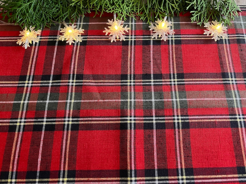 May include: Red and black plaid tablecloth with a string of white snowflake lights across the top.