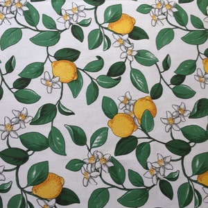 May include: White fabric with a repeating pattern of green leaves, white flowers, and yellow lemons.