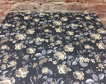 Può includere: Tessuto nero con un motivo floreale con rose beige e grigie e fiori più piccoli. Il tessuto ha una leggera lucentezza.