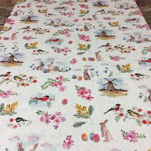 May include: White tablecloth with a repeating pattern of bunnies, birds, windmills, flowers, and Easter eggs. The pattern is in shades of pink, yellow, blue, and green.
