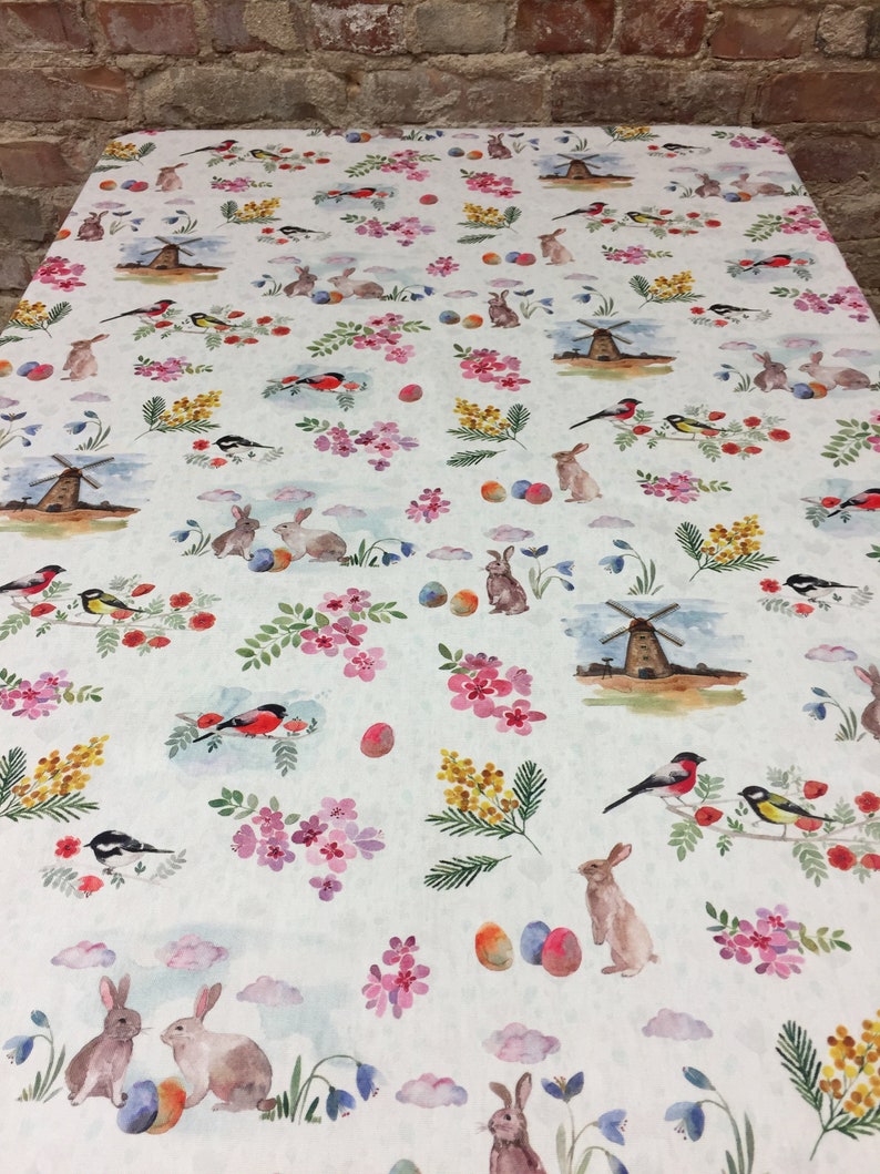 May include: White tablecloth with a repeating pattern of bunnies, birds, windmills, flowers, and Easter eggs. The pattern is in shades of pink, yellow, blue, and green.