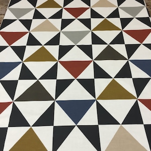 Puede incluir: Tela blanca con un patrón geométrico de triángulos negros, marrones, beige, rojos y azules.