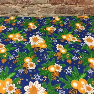 May include: Blue tablecloth with a festive Christmas pattern featuring white poinsettia flowers, orange baubles, green pine branches, and gold pine cones on a dark blue background.