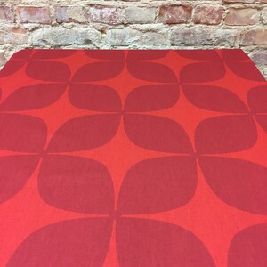 Puede incluir: Mantel rojo con un patrón geométrico de círculos y hojas superpuestos. El mantel tiene una superficie texturizada.