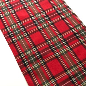 May include: Red and green plaid table runner with a white background. The runner has a woven texture and is made of cotton.