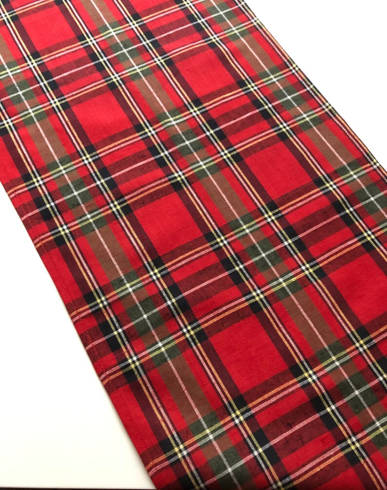 May include: Red and green plaid table runner with a white background. The runner has a woven texture and is made of cotton.