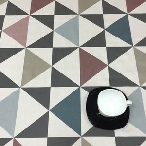 Puede incluir: Una taza de café blanca sobre un platillo negro, colocada sobre una superficie con un patrón geométrico. El patrón presenta triángulos en tonos grises, azules y malva sobre un fondo blanco. El diseño crea una estética moderna y abstracta.