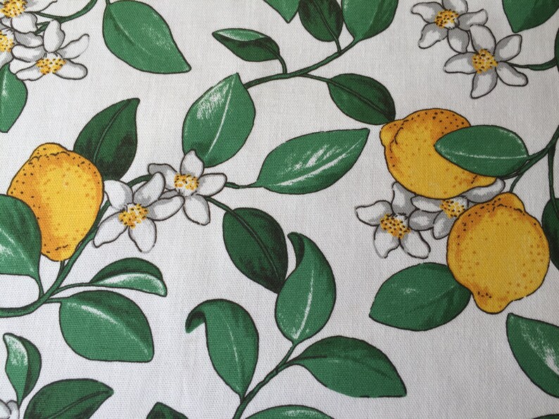 May include: White fabric with a repeating pattern of green leaves, white blossoms, and yellow lemons.