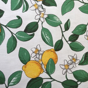 May include: White fabric with a repeating pattern of green leaves, white flowers, and yellow lemons.