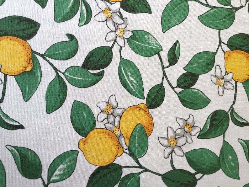 May include: White fabric with a repeating pattern of green leaves, white flowers, and yellow lemons.