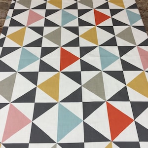 Peut inclure: Un tissu blanc avec un motif géométrique de triangles noirs, gris, bleu clair, rose et jaunes.