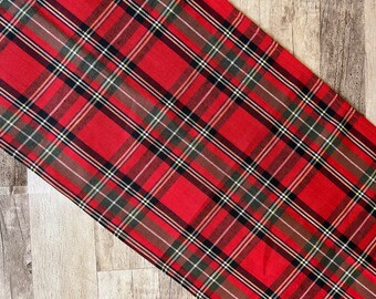 May include: Red, black, green, and white plaid table runner. The runner has a woven texture and is made of fabric.