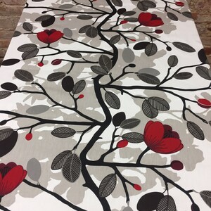 May include: A white tablecloth with a floral design featuring red flowers, black branches, and gray leaves. The pattern is repeated across the fabric, creating a nature-inspired aesthetic. The tablecloth is likely made of a durable material.