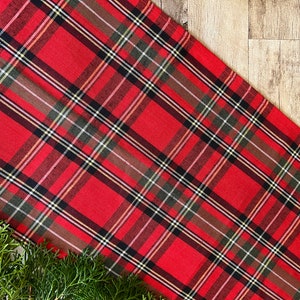May include: Red and green plaid table runner with a white and yellow plaid pattern. The runner is made of a soft, woven fabric.
