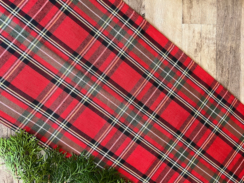 May include: Red and green plaid table runner with a white and yellow plaid pattern. The runner is made of a soft, woven fabric.