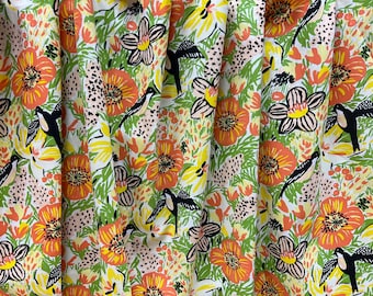 Peut inclure: Un tissu blanc avec un motif répétitif de fleurs orange, jaunes et vertes et d'oiseaux noirs. Les fleurs ont des centres noirs et des accents blancs.