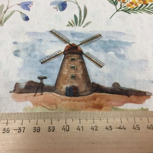 May include: A watercolor illustration of a brown windmill with white blades against a blue sky background. The windmill is surrounded by green grass and brown dirt. The image is printed on a white fabric with a ruler measuring 34 to 48 inches.