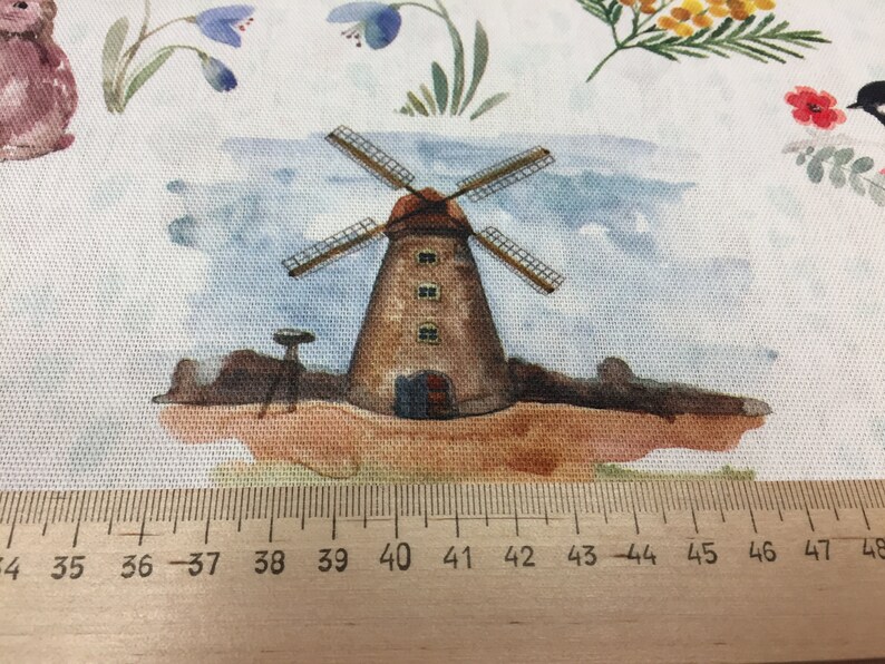 May include: A watercolor illustration of a brown windmill with white blades against a blue sky background. The windmill is surrounded by green grass and brown dirt. The image is printed on a white fabric with a ruler measuring 34 to 48 inches.